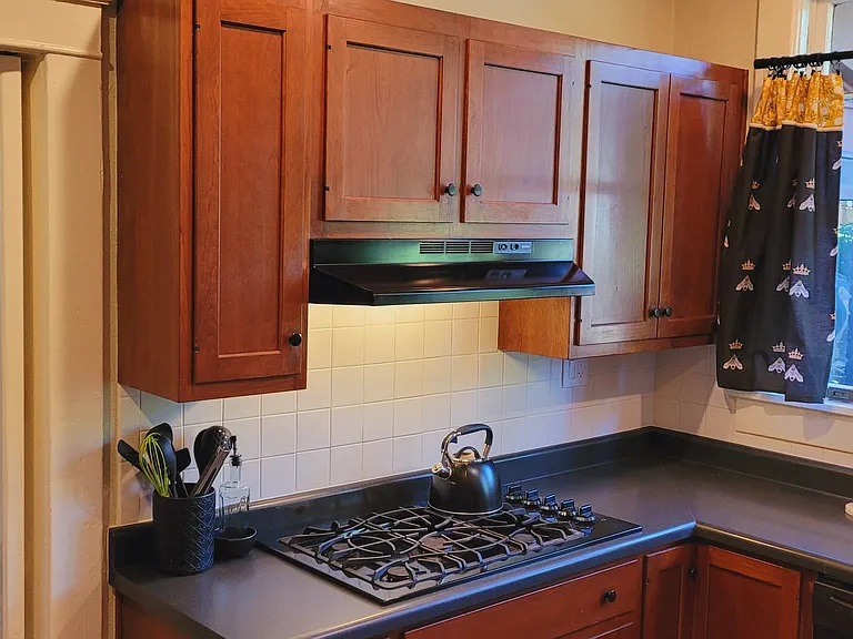 Kitchen cabinets above gas cooktop. Custom curtains cover windows looking out onto the private patio area