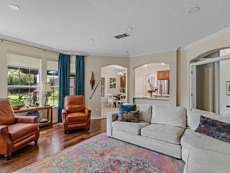 Spacious living area featuring wood-finish flooring, numerous windows with blinds, architectural archways, and recessed lighting