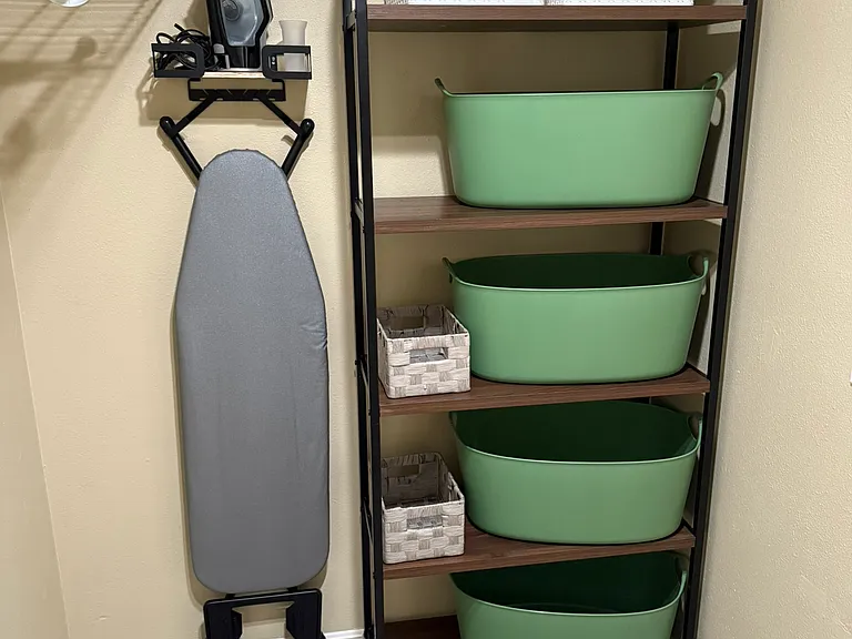 Other portion of walk-in closet with ironing board and a shelf with baskets