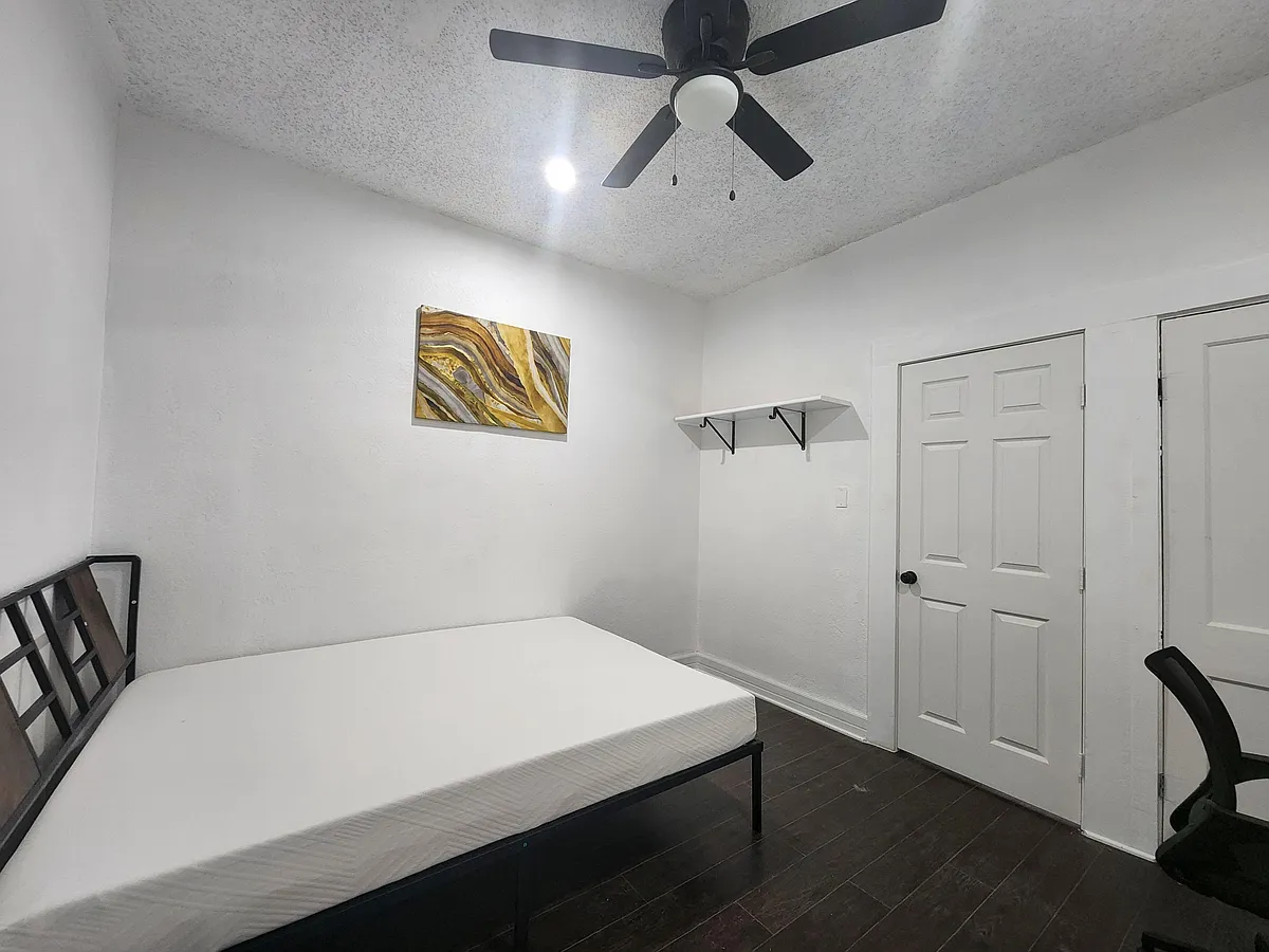 Private bedroom with dark wood-style floors, ceiling fan with light, and a wall shelf for added storage and display. - E Drexel Ave