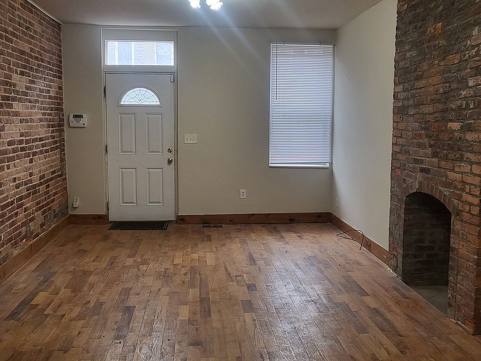 Living room and front door. Hardwood flooring, exposed brick, and fireplace FOR SHOW ONLY (the city no longer allows these to be in use; flue is sealed).