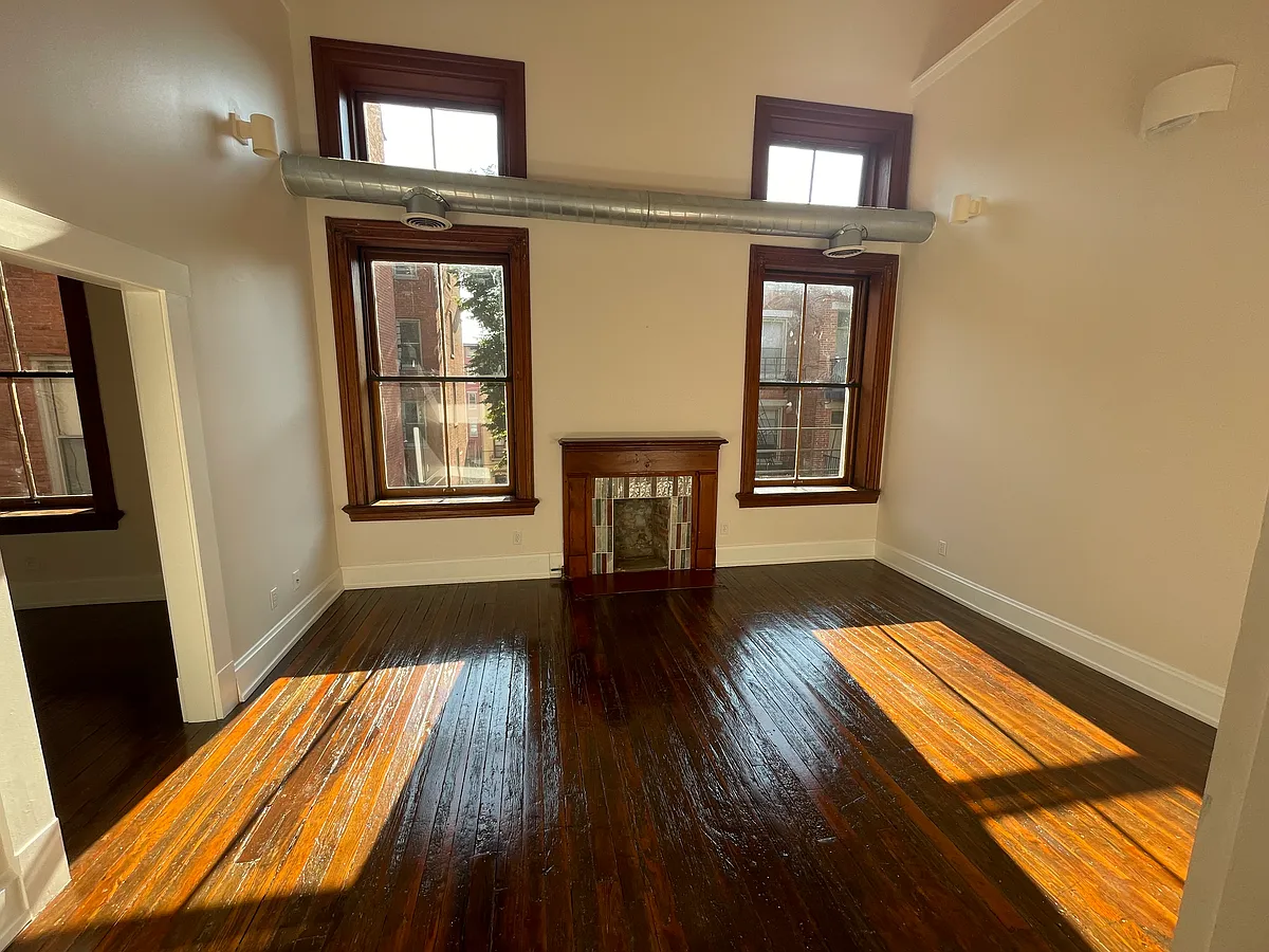 Morning sun on two-story living room with four windows and original ductwork. Artisan tile fireplaces weaves in colors from nearby dining room revealing original colors from years past - 1222 Race St #5