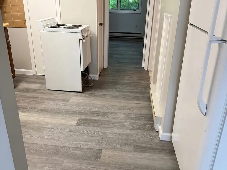 Kitchen entryway featuring a white stove and refrigerator, highlighted by crisp, freshly painted walls and beautiful new LVP flooring that extends seamlessly down the hallway.
