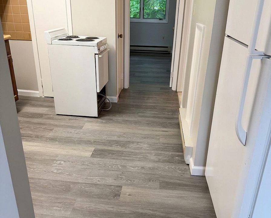 Kitchen entryway featuring a white stove and refrigerator, highlighted by crisp, freshly painted walls and beautiful new LVP flooring that extends seamlessly down the hallway.