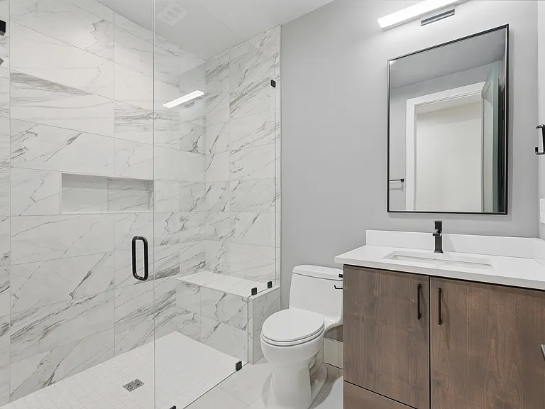 Modern bathroom walk-in glass shower, marble-style tile, and sleek vanity.