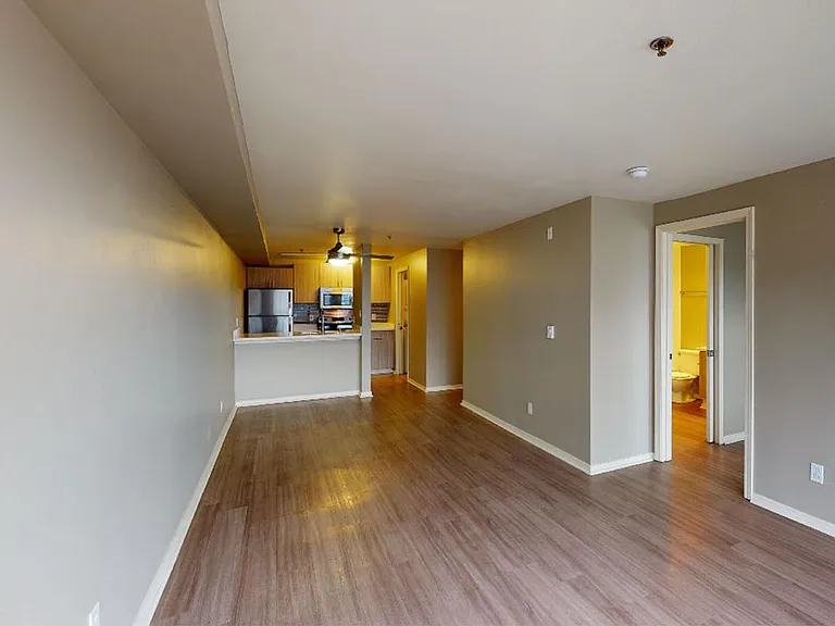 Apartment kitchen with stainless steel appliances, dining and living room with wood-style flooring.