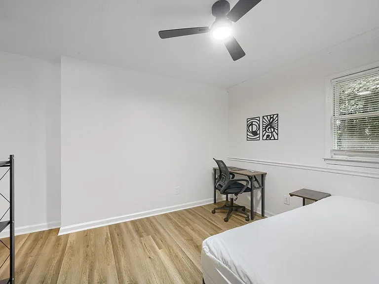 Private bedroom with wood-look flooring, ceiling fan, and a window with blinds, plus space for a desk and bed.