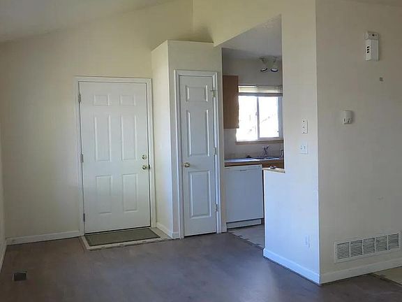 Looking at the front door an kitchen from the Dining/Living Room which has vaulted ceilings. The hall goes into the laundry closet and garage.