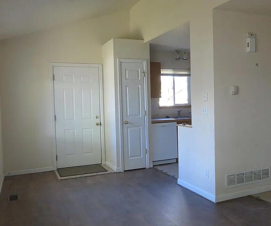 Looking at the front door an kitchen from the Dining/Living Room which has vaulted ceilings. The hall goes into the laundry closet and garage.