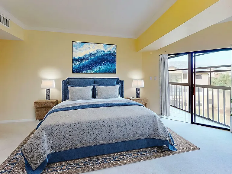 Elegant bedroom with soothing yellow walls, featuring a plush blue headboard, stylish bedding, and large window offering abundant natural light.