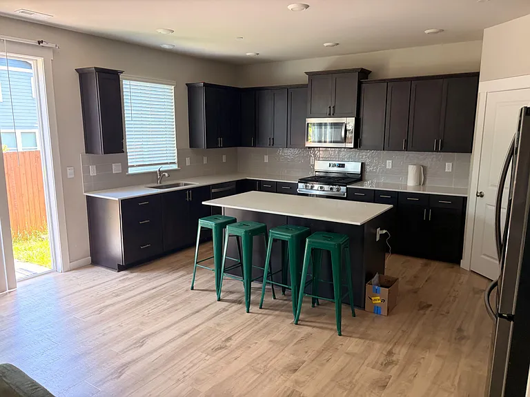 Open kitchen with dark cabinetry, stainless appliances, and a large island with seating plus backyard access.