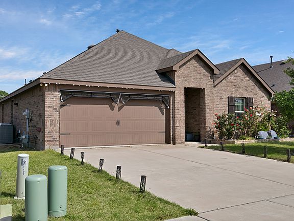 View of the front of the home with a front yard, a garage, a concrete driveway, brick siding, and a roof