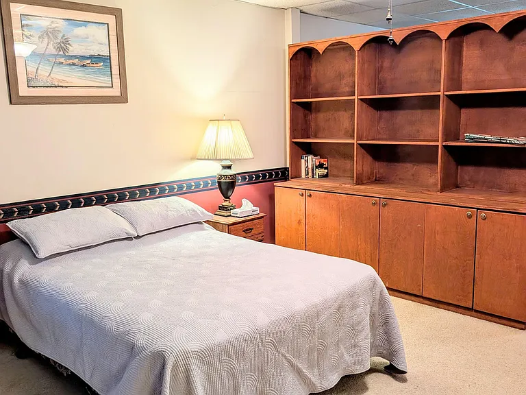 Furnished bedroom with a full bed, bedside table, ceiling fan, and built-in shelving and storage for easy organization.