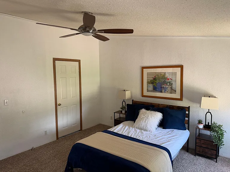 Furnished bedroom with ceiling fan, bedside tables, and soft carpet flooring for comfortable everyday living.