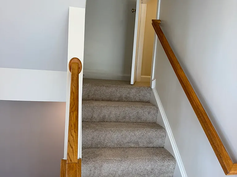 Stairs to the top floor with a door partially opened door to a storage area