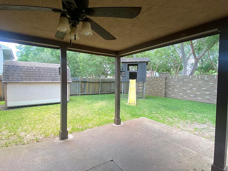 Left area of backyard including large covered porch, outdoor storage unit, and play house