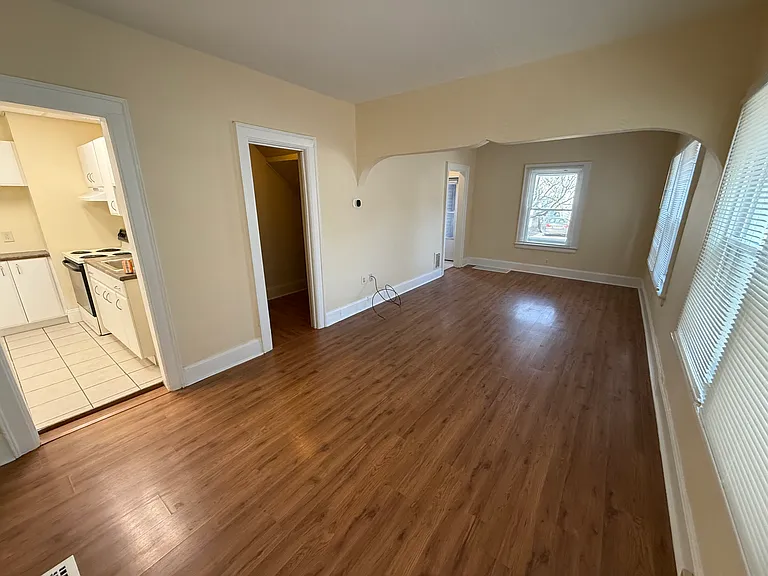 Living room, looking forward to the front door, with forward window overlooking the front porch. Living room has a small closet/storage area. View to kitchen shown.