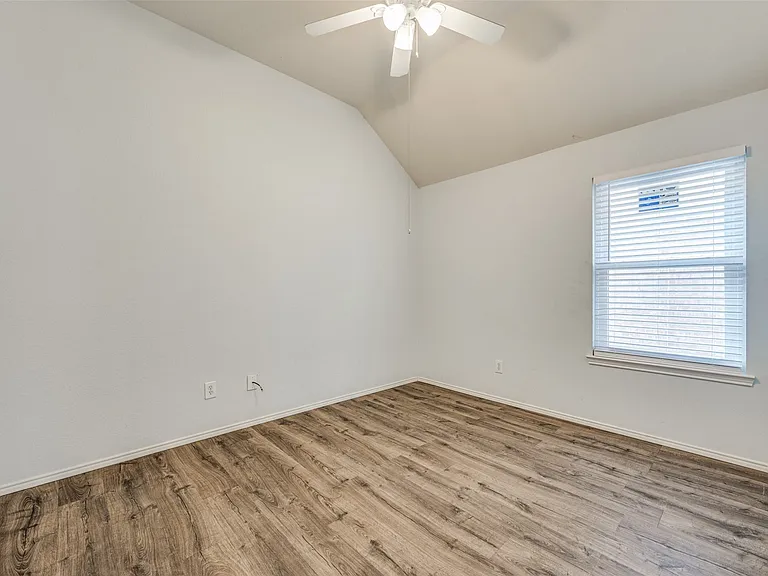 Room featuring vaulted ceilings, wood-finish flooring, a window with horizontal blinds, and a ceiling fan with integrated lighting