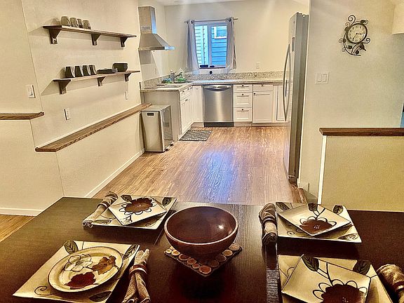 View of fully stocked kitchen (new appliances including Multi-purpose countertop oven/air fryer/toaster/slow cooker etc. And two burner induction stove top) from dining and granite bar area looking over living room- TV can be viewed from dining area
