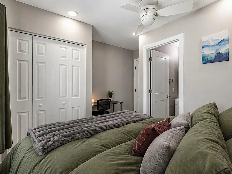 Well-appointed bedroom with a full bed, two large windows with a mini fridge and wall A/C.