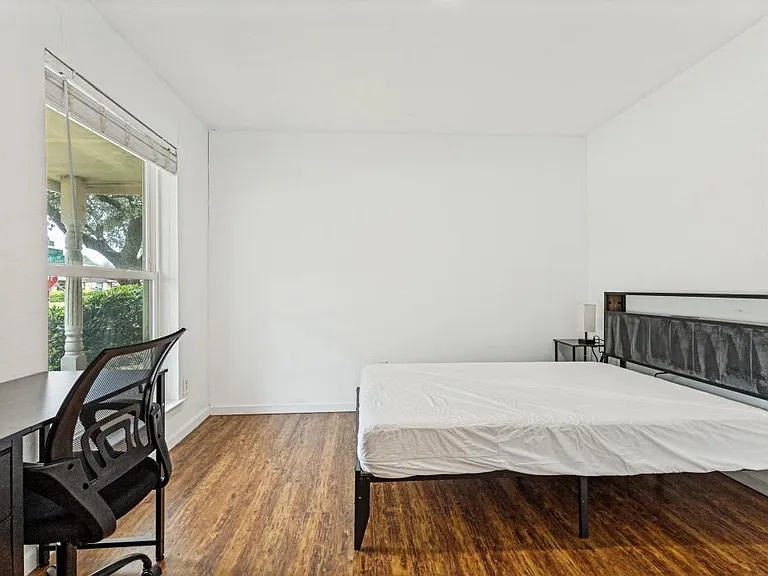 Private bedroom with a large window, wood-style flooring, and space for a full bed plus a work desk.