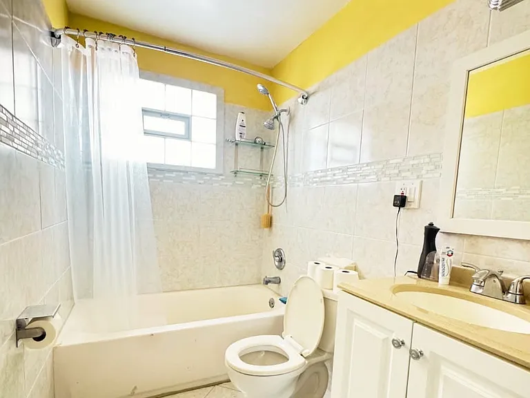 A spacious bathroom featuring clean, heated tile flooring and beautifully maintained white tiled walls. It includes a large vanity mirror, adding both functionality and a bright, open feel to the space.