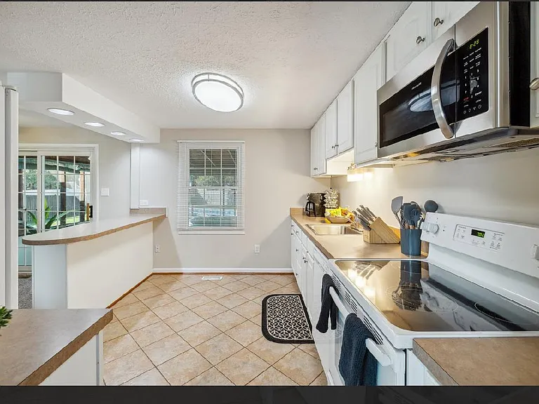 Efficient galley kitchen with ample white cabinetry, laminate counters, and a full appliance set for everyday cooking.