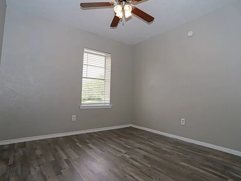 Spacious bedroom with large window and wood-style flooring.