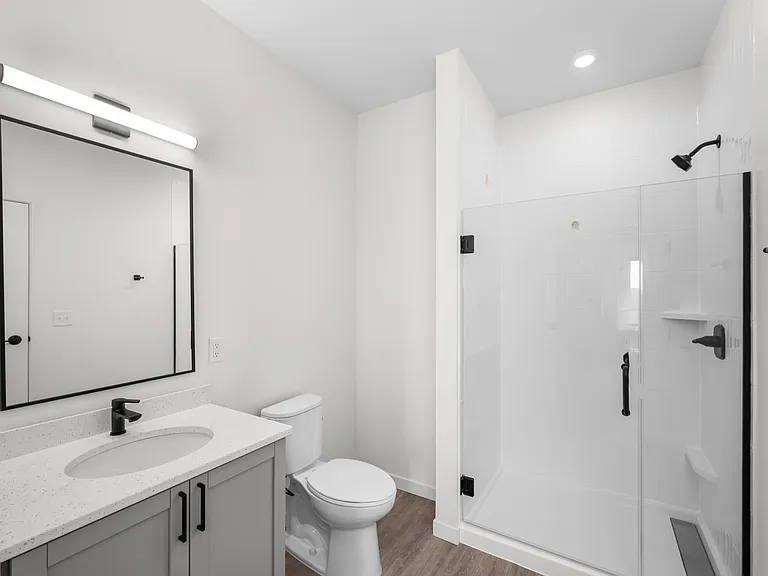 Modern bathroom with sleek white vanity topped with a quartz countertop, elegant black fixtures, and a spacious glass-enclosed shower. Modern bathroom with sleek white vanity topped with a quartz countertop, elegant black fixtures, and a spacious glass-en