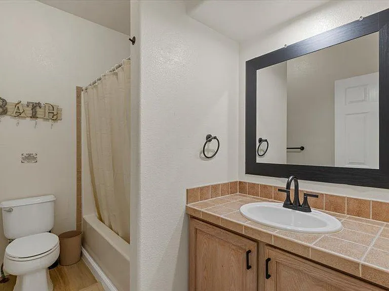 Full bathroom with tub/shower combo, tile countertop vanity, and a large framed mirror for daily routines.