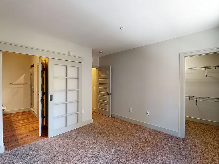 Spacious apartment bedroom with large closet, attached bathroom and plush carpet flooring.
