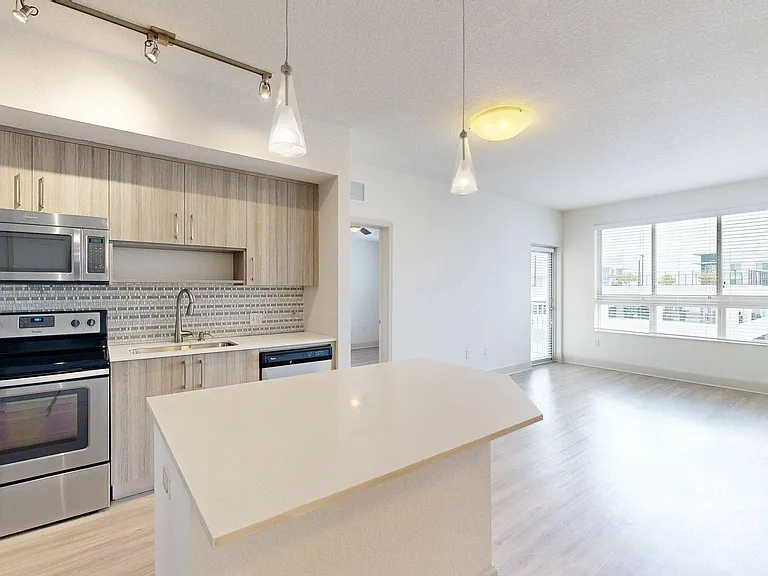 Apartment kitchen with stainless steel appliances, light counters, and wood style floor.