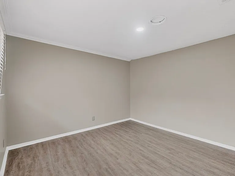 A bedroom with warm hardwood floors and a window, creating a bright and airy atmosphere.