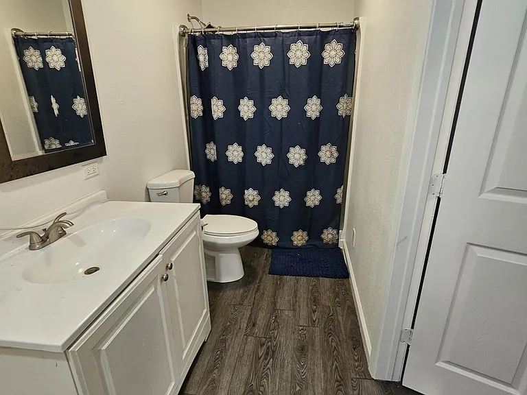 Clean full bathroom with a wide vanity, framed mirror, and tub/shower combo, plus durable wood-look flooring.