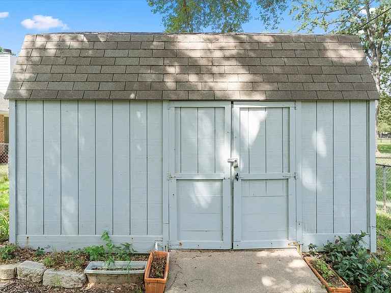 Exterior storage shed with vertical panel siding, double barn doors, and an asphalt shingle roof