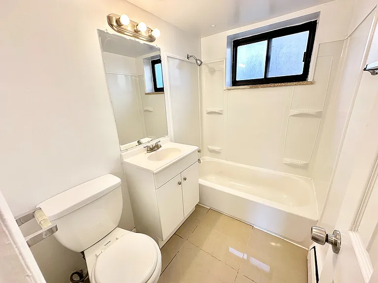 Bright and modern bathroom featuring a sleek white vanity, elegant bathtub, and ample natural light through the stylish window.