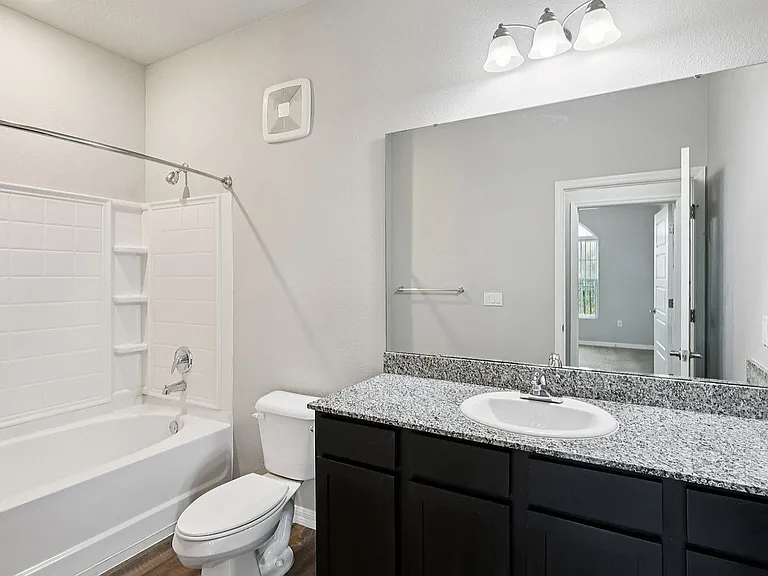 Elegant bathroom with granite countertop, large mirror, and modern lighting fixtures, offering a serene retreat.