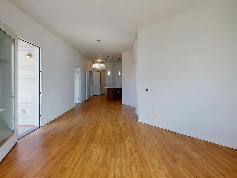 Apartment kitchen with stainless steel appliances, dining and living room with wood-style flooring.