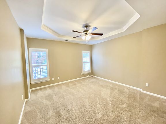 Spacious main level primary bedroom with tray ceiling, ceiling fan, plush carpet, and plantation shutters. Bright and private.