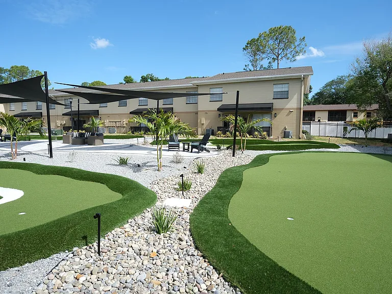 Charming outdoor area featuring a scenic putting green, elegant seating under shade sails, and lush palm trees for a relaxing atmosphere.