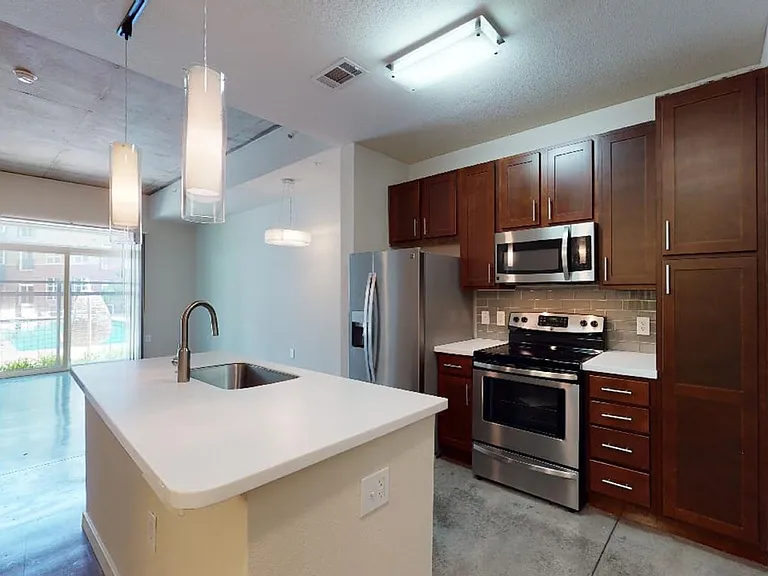 Apartment kitchen with stainless steel appliances, dining and living room with polished concrete flooring.