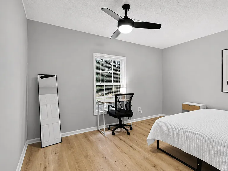Private bedroom with vinyl plank flooring, a new ceiling fan, and a large window plus desk and chair.