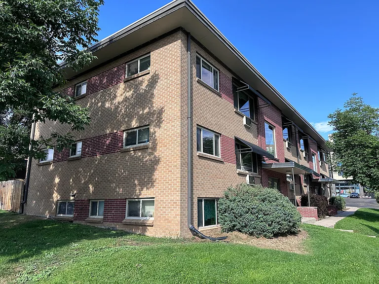 Charming brick apartment building with lush greenery and a welcoming entrance, perfect for urban living.