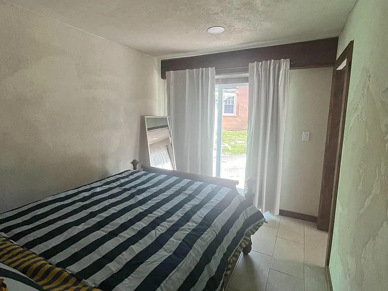 Furnished bedroom with tiled floors, ceiling lighting, and sliding glass doors with curtains for easy outdoor access.