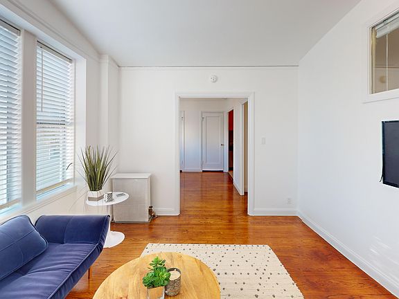 Serene and well-organized living room, dominated by a large window, furnished with a couch and a coffee table, a flat screen TV mounted on the wall