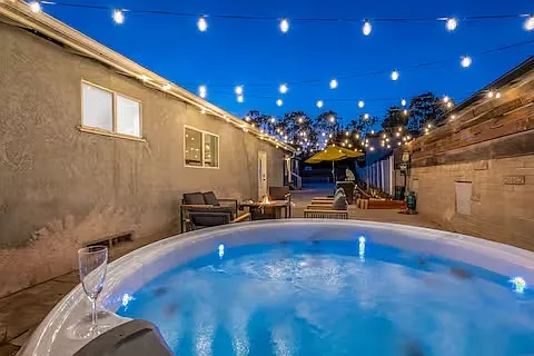 String lights elegantly drape across the patio, casting a warm glow as the sun sets into a beautiful gradient sky while you soak your cares away in the hot tub under the stars.