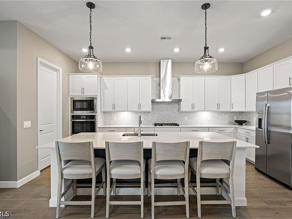 Kitchen with a large quartz island seating five, gas range under a vented hood, built-in wall ovens and white cabinetry, Punta Gorda, Florida