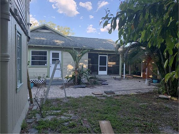 Back of house showing back door and back door of screened porch. Pavers on patio and shaded yard. Detached garage and apartment above it are rented separately.