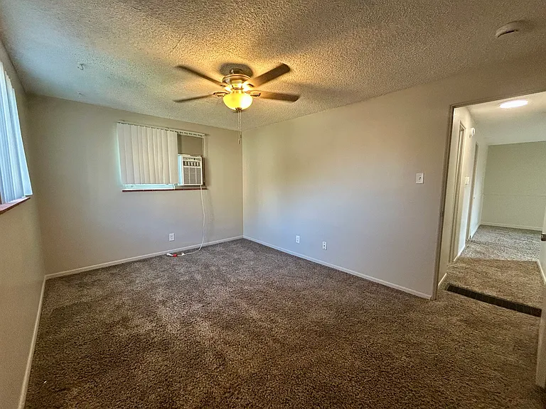 Cozy bedroom with plush carpeting, ceiling fan, and natural light from a window air conditioner unit. Cozy bedroom with plush carpeting, ceiling fan, and natural light from a window air conditioner unit.