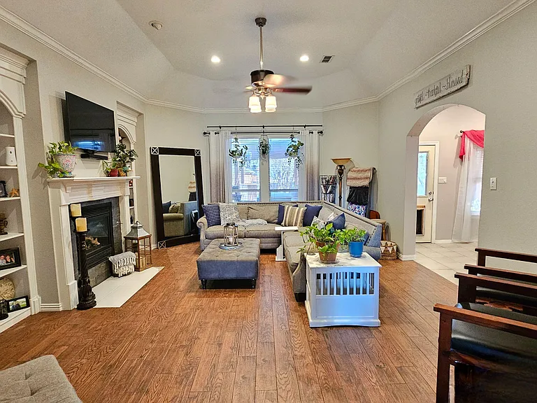 Spacious living room with hardwood floors, built-in shelving, a fireplace, and ample seating around a large window.